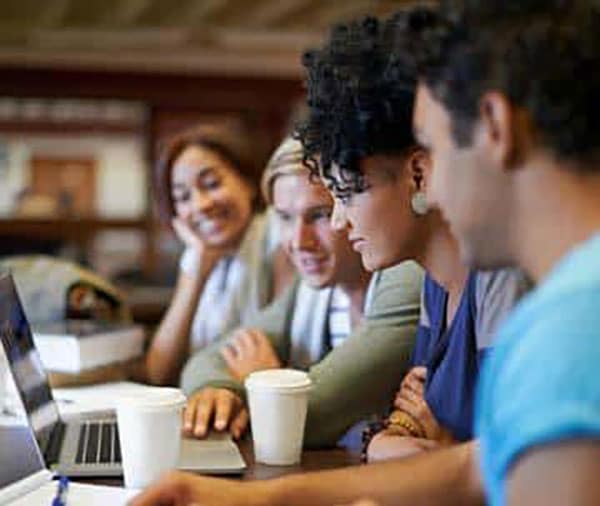 Four people sitting at PC, looking at screen.