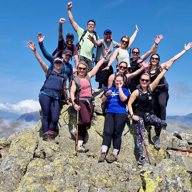 Group-of-people-on-top-of-mountain-with-arms-in-air-to-celebrate-reaching-top.